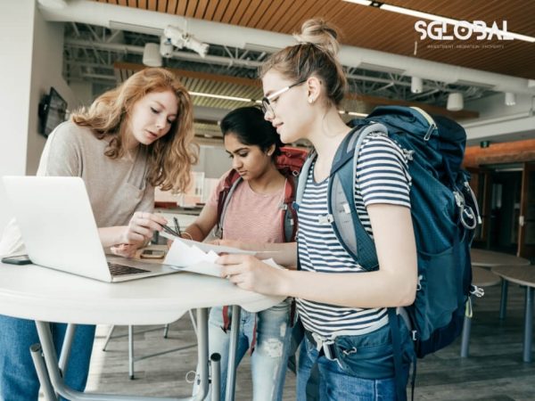 Hai bạn sinh viên cùng nhau xem thông tin du học trên laptop, trong không gian trường học hiện đại.