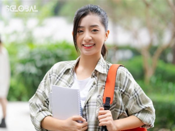 Nữ sinh Việt Nam tươi cười, cầm sách và balo, sẵn sàng cho chương trình du học nghề ở Đức.