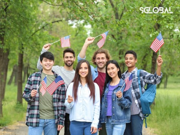 Nhóm sinh viên du học Mỹ cầm cờ chụp ảnh kỷ niệm tại công viên, thể hiện tinh thần quốc tế.