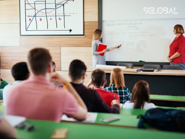 Giảng viên đang giảng bài trong lớp học đại học, có biểu đồ kinh tế phía sau, phù hợp với các ngành hot như Data Analyst, Kinh doanh, IT.