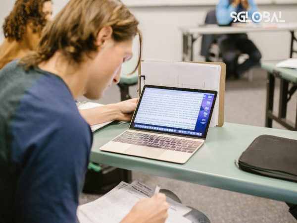 Nam sinh viên đang viết bài luận học bổng với laptop và vở ghi chép trong lớp học.