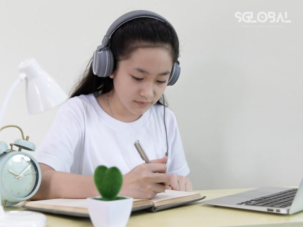 Học sinh nữ đeo tai nghe, ghi chép bài học tiếng Đức tại nhà, chuẩn bị cho du học nghề ở Đức.
