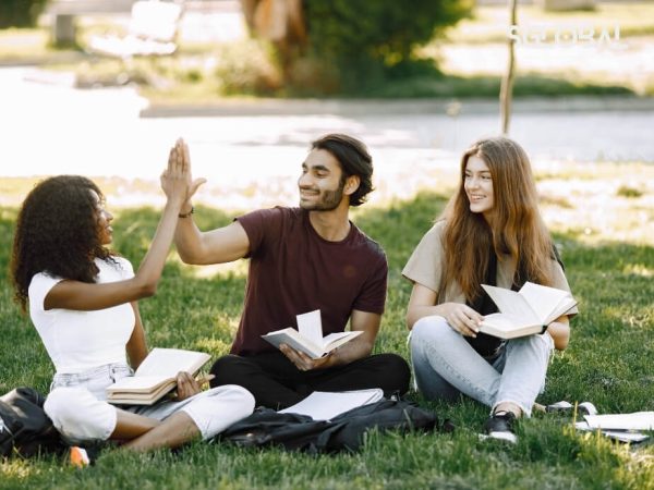 Hai sinh viên quốc tế đang ngồi ngoài trời, vui vẻ high-five – đại diện cho cuộc sống du học tiết kiệm mà chất lượng.