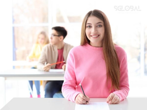 Nữ sinh mặc áo hồng rạng rỡ ngồi trong lớp học, thể hiện sự tự tin và hài lòng sau khi đạt học bổng.